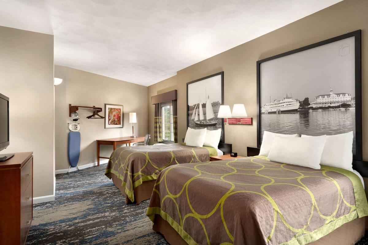 A hotel room with two beds, a desk, a chair, a TV, and a large window.