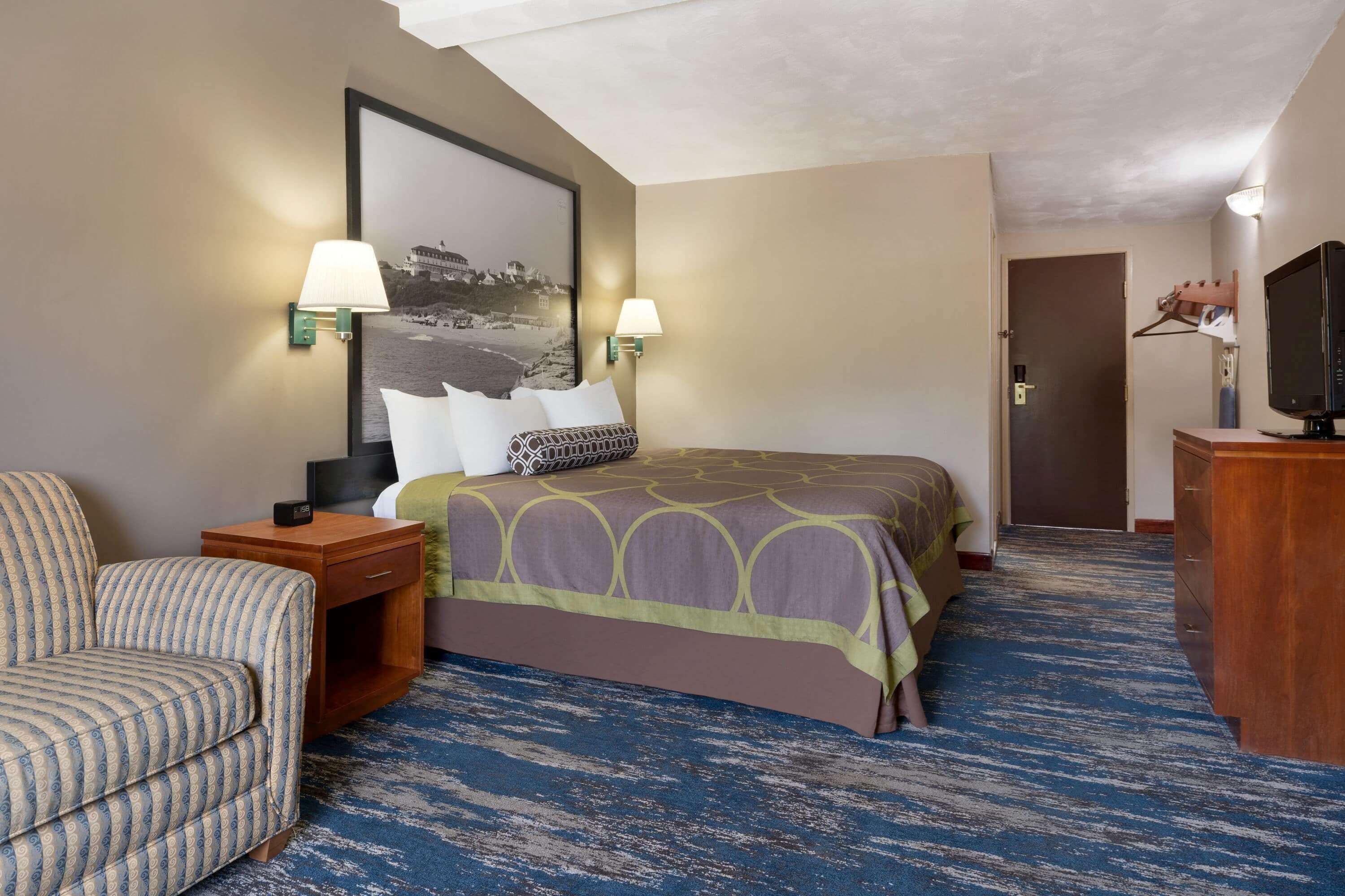 A hotel room with a bed, a chair, a desk, and a television.