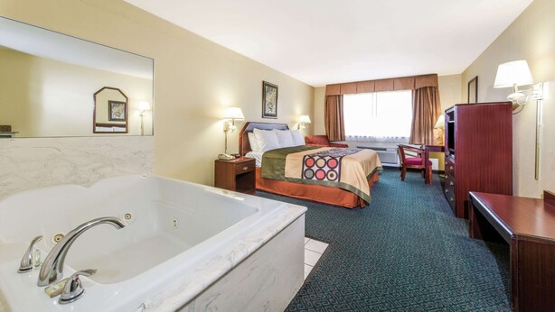 Ein Hotelzimmer mit einer großen Badewanne, einem Bett mit einer farbenfrohen Decke, einem Schreibtisch und einem Sessel.