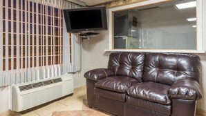 A living room with a leather sofa, a flat-screen TV mounted on the wall, and a window with blinds. - Super 8 by Wyndham Old Saybrook (Old Saybrook)