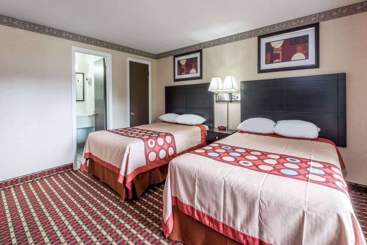 A hotel room with two beds, a nightstand with lamps, a door, and a patterned carpet.
