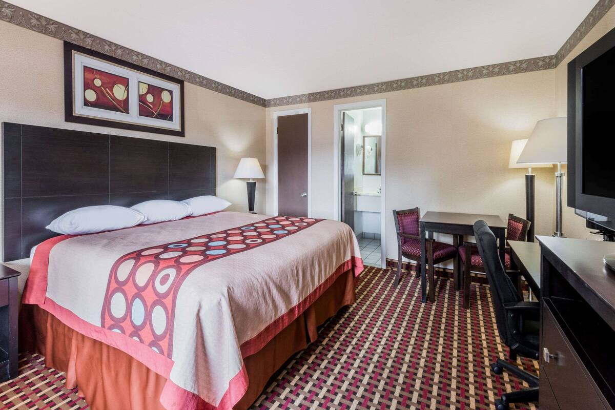A hotel room with a large bed, a desk, a chair, a TV, and a door leading to a bathroom.