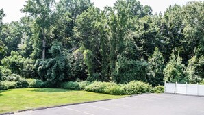 A parking lot with a grassy area and dense trees in the background. - Super 8 by Wyndham Old Saybrook (Old Saybrook)