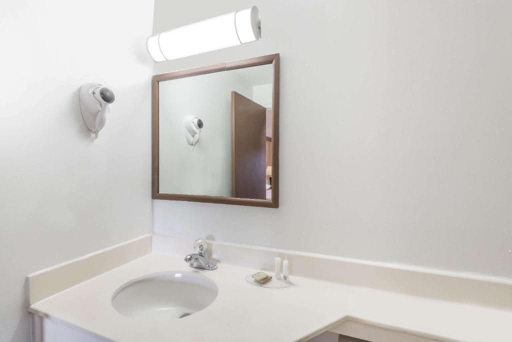 Een badkamer met een wastafel, spiegel, zeepdispenser en een lamp.