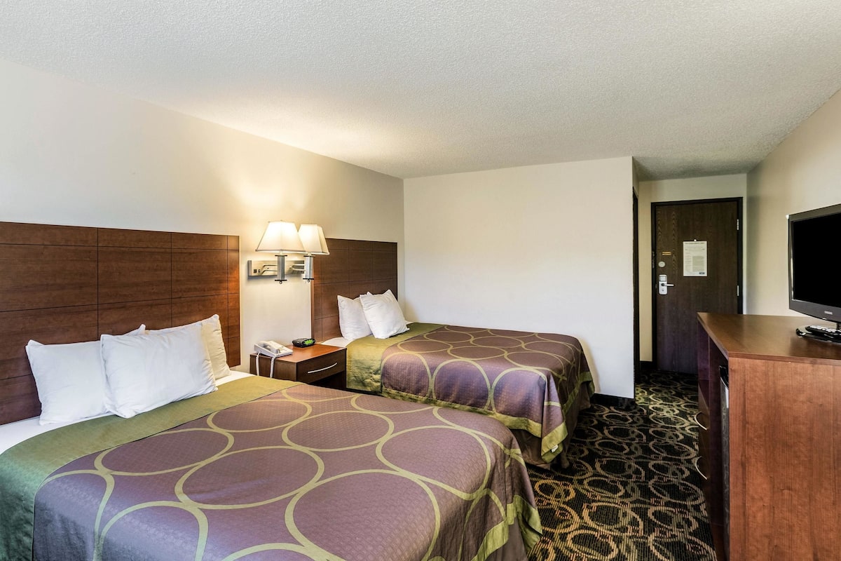 A hotel room with two beds, a desk, a television, and a lamp.