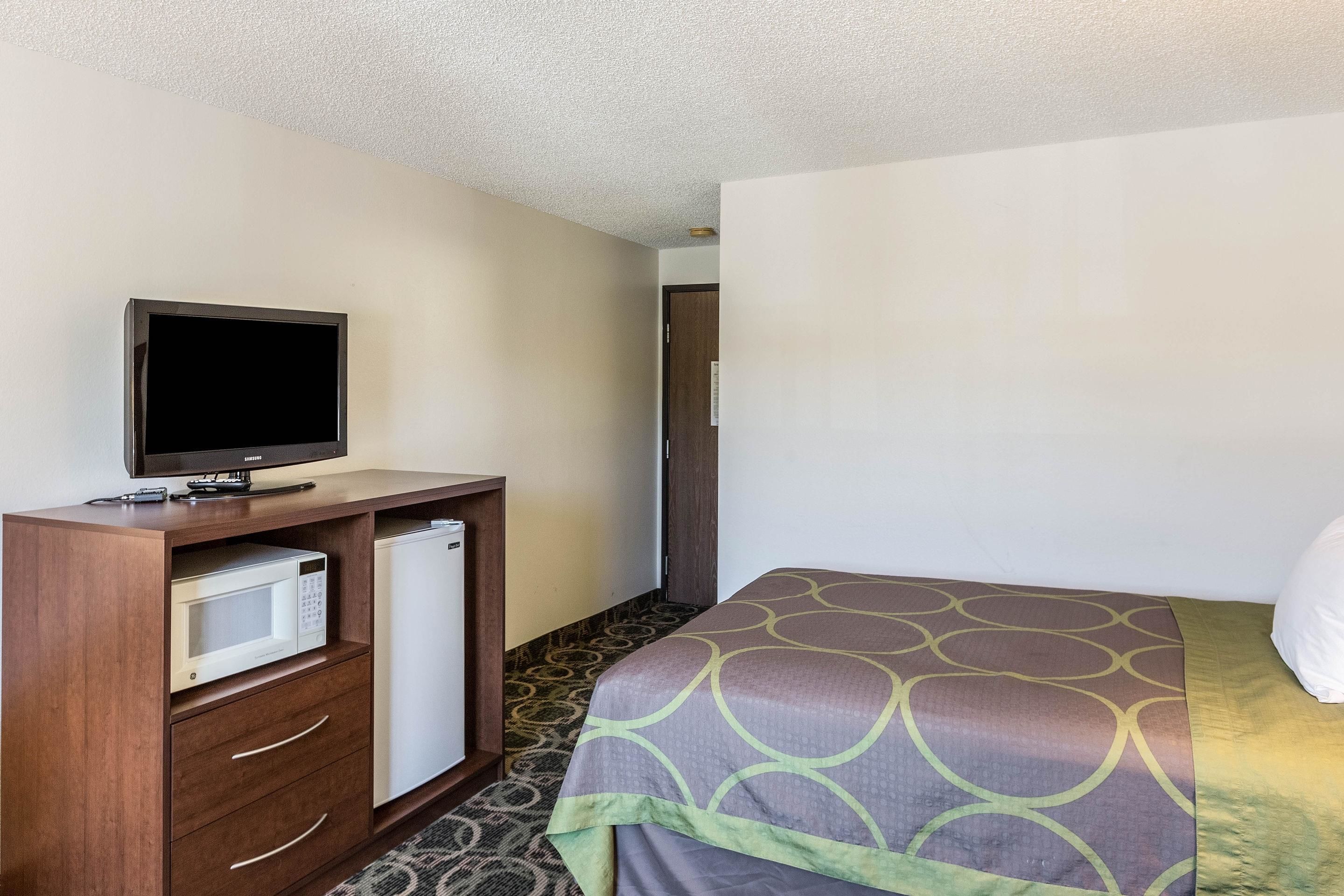 Een hotelkamer met een bed, een televisie op een houten dressoir, een magnetron en een koelkast.
