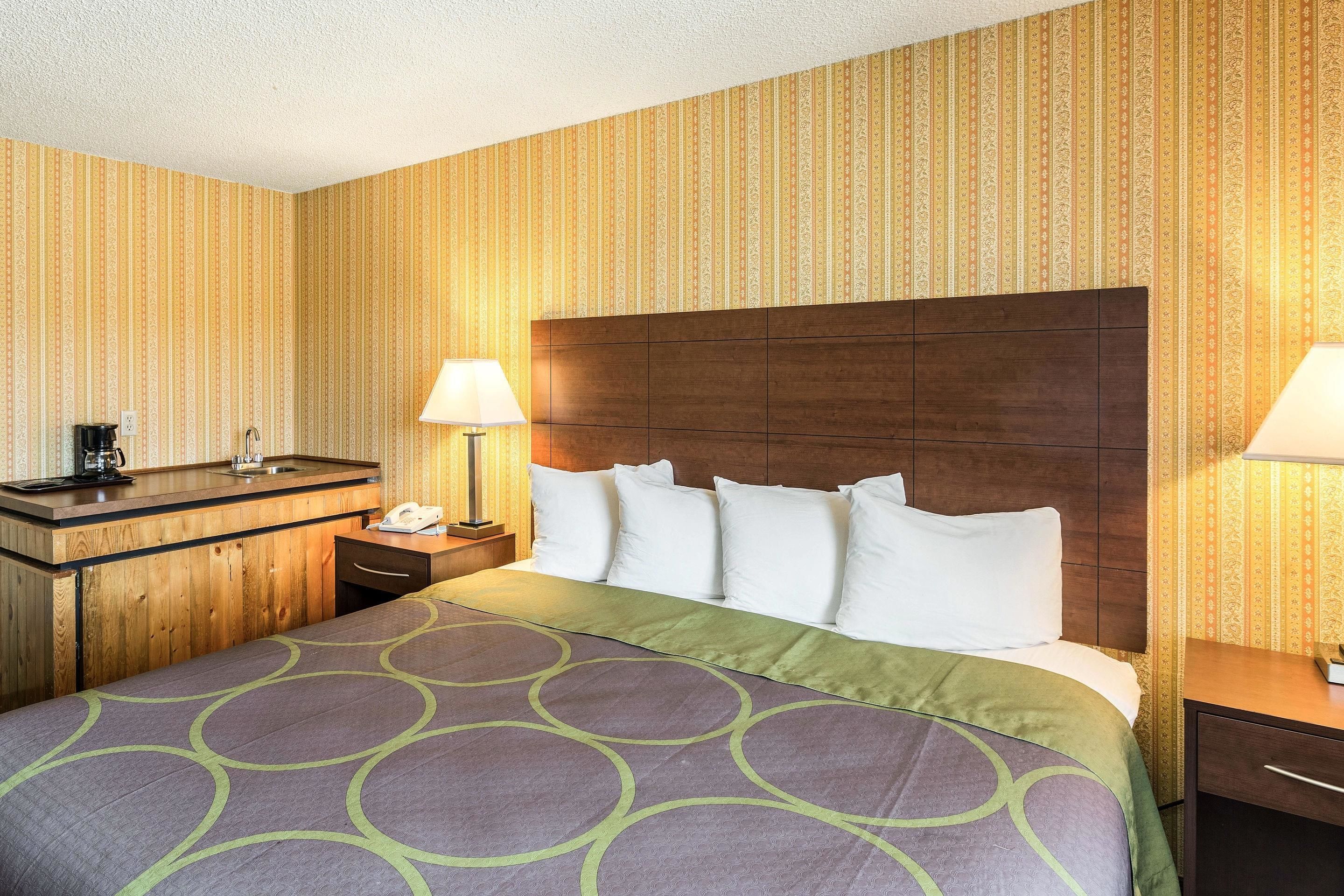 A hotel room with a wooden headboard, a bed with a patterned bedspread, a bedside table with a lamp, and a small desk with a telephone.