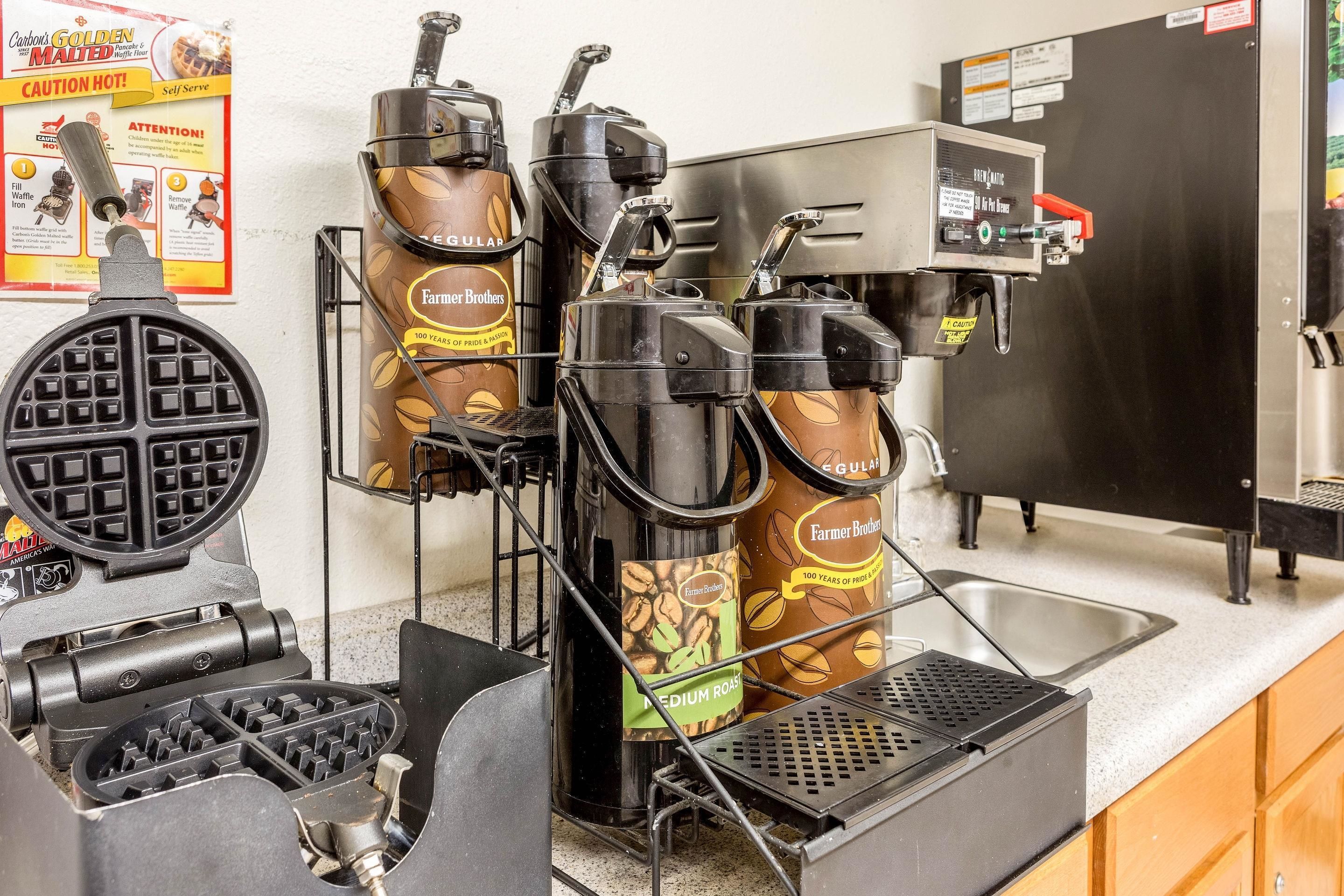 Een koffiehoek met een wafelijzer, twee koffiezetapparaten en een spoelbak.