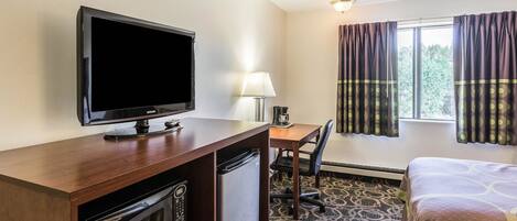 Ein Hotelzimmer mit Fernseher, Schreibtisch, Stuhl und Bett.