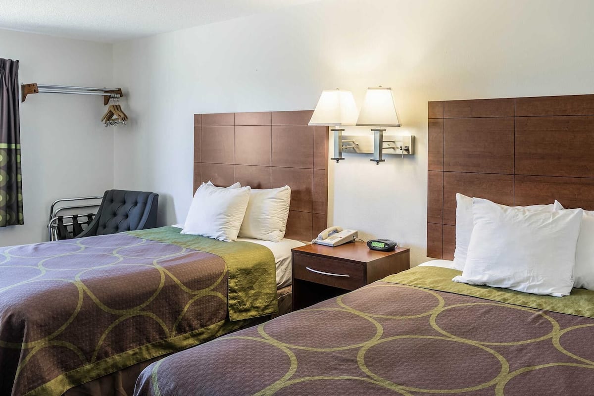 A hotel room with two beds, a chair, a desk, a lamp, and a telephone.