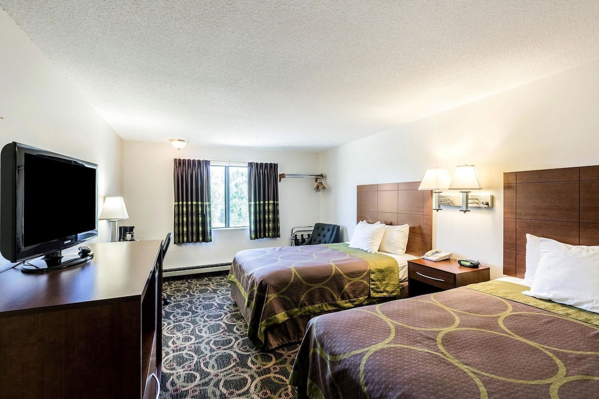 A hotel room with two beds, a TV, a desk, a lamp, and a window with curtains.