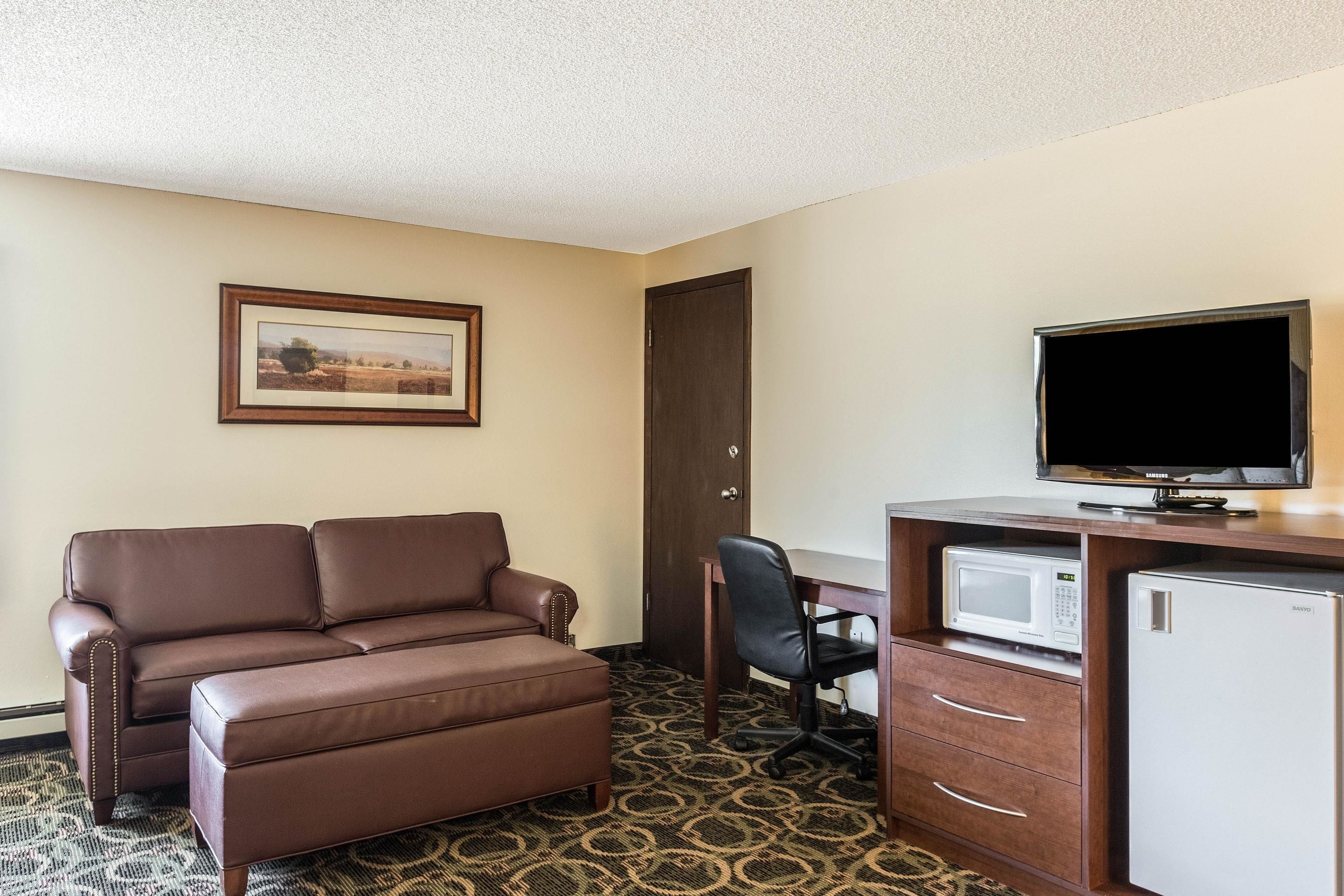 Habitación de hotel con un sofá de cuero marrón, un escritorio con una silla, un televisor, un microondas y un refrigerador.