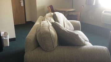 A hotel room with a sofa, a table, a lamp, and a window with curtains.