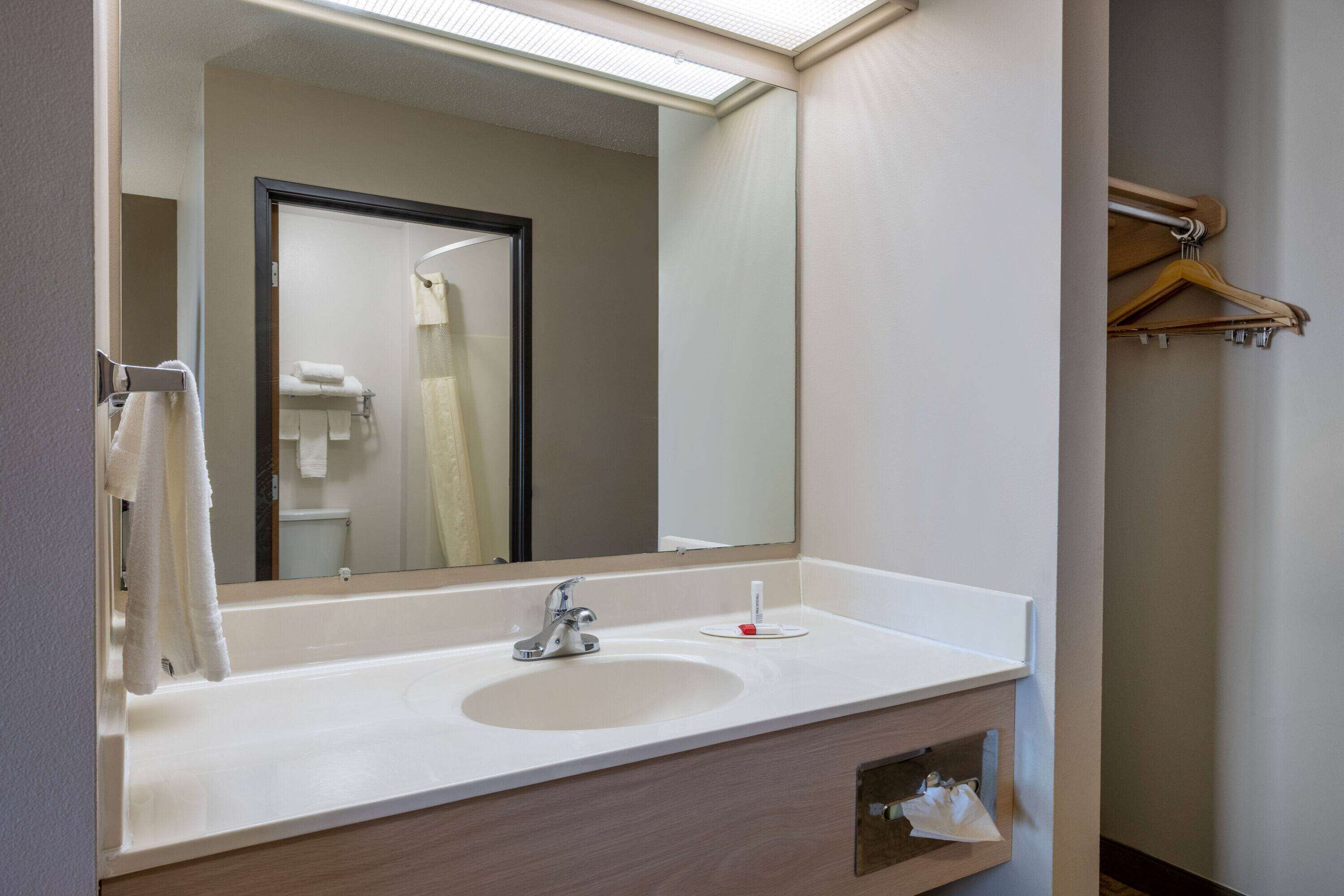 Un baño de hotel con un espejo grande, un lavamanos y un perchero para toallas.