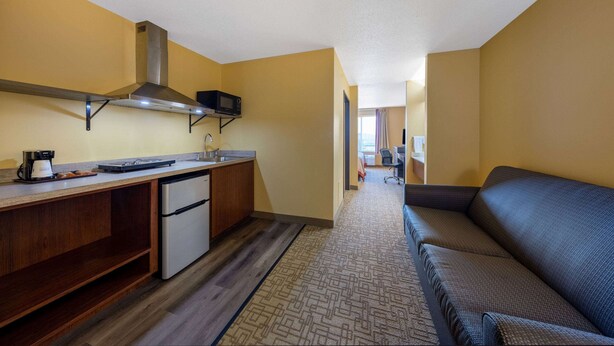 A compact kitchen with a microwave, stove, and refrigerator. A sofa is positioned in the living area, and a window provides natural light. - Super 8 by Wyndham Jackson MN (Jackson)