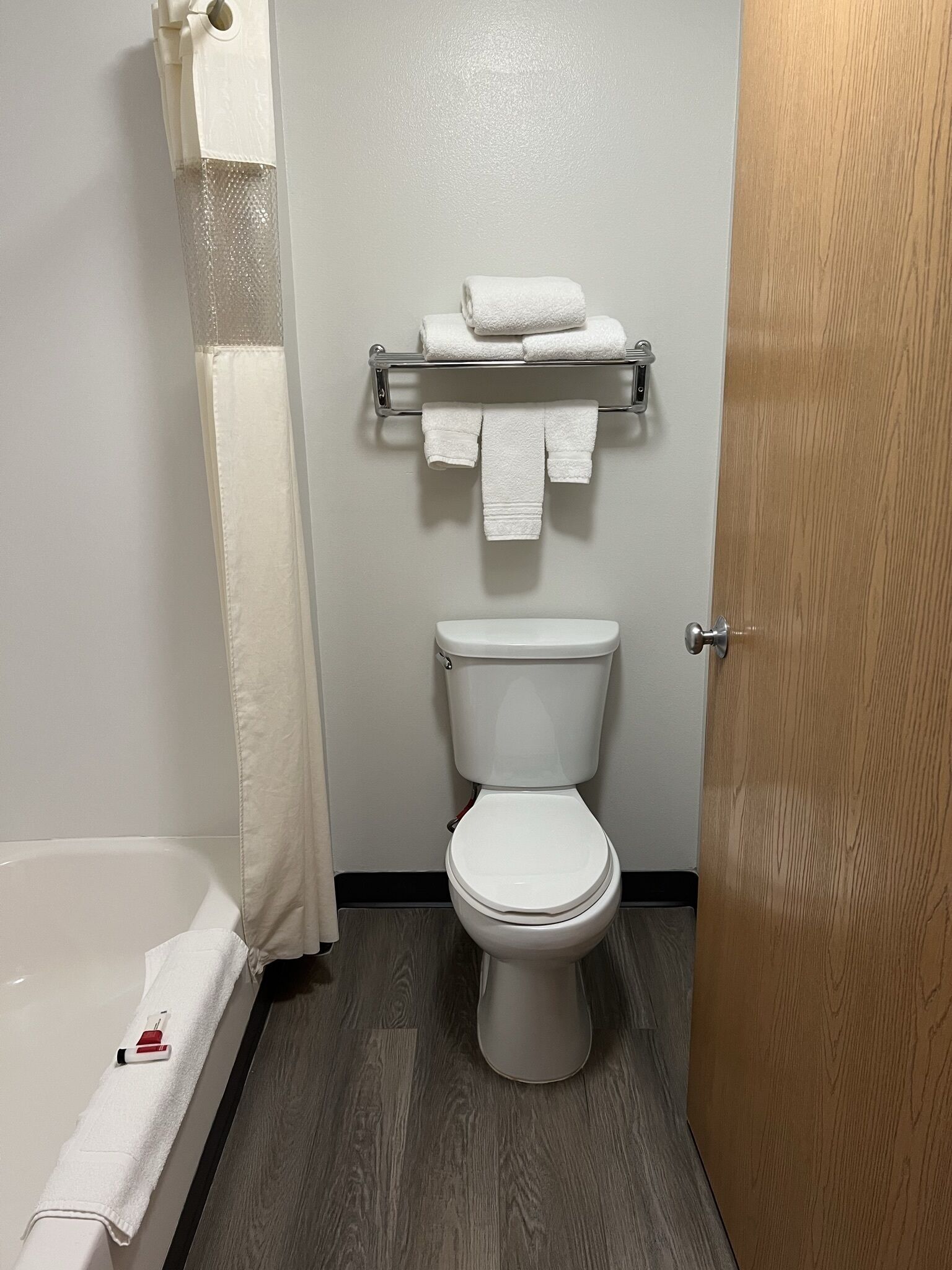 A bathroom with a toilet, a towel rack with towels, a shower curtain, and a wooden door.