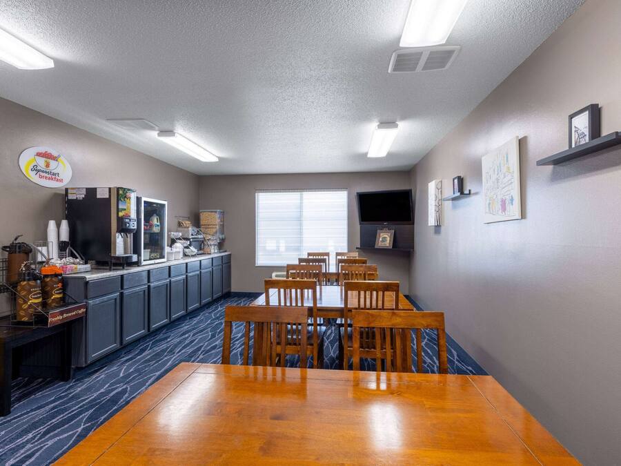A breakfast area with a long wooden table, chairs, a coffee station, and a television on the wall.