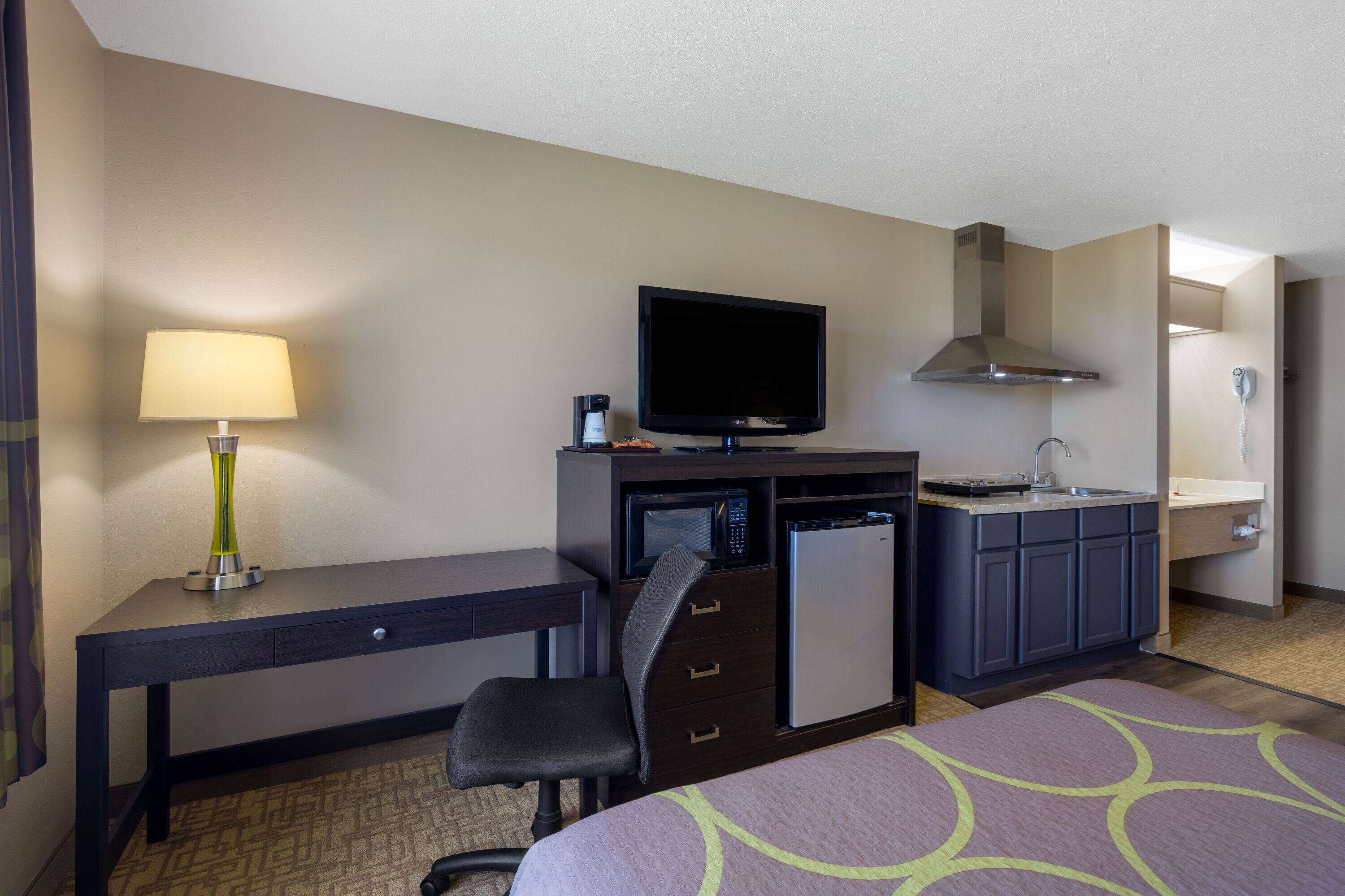 A hotel room with a bed, a desk with a lamp, a television, a mini-fridge, a microwave, a sink, and a mirror.