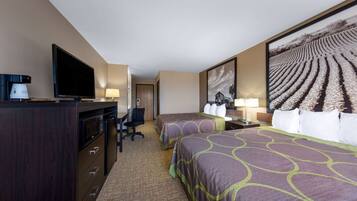 A hotel room with two beds, a TV, a desk with a chair, a coffee maker, and a large framed picture on the wall.