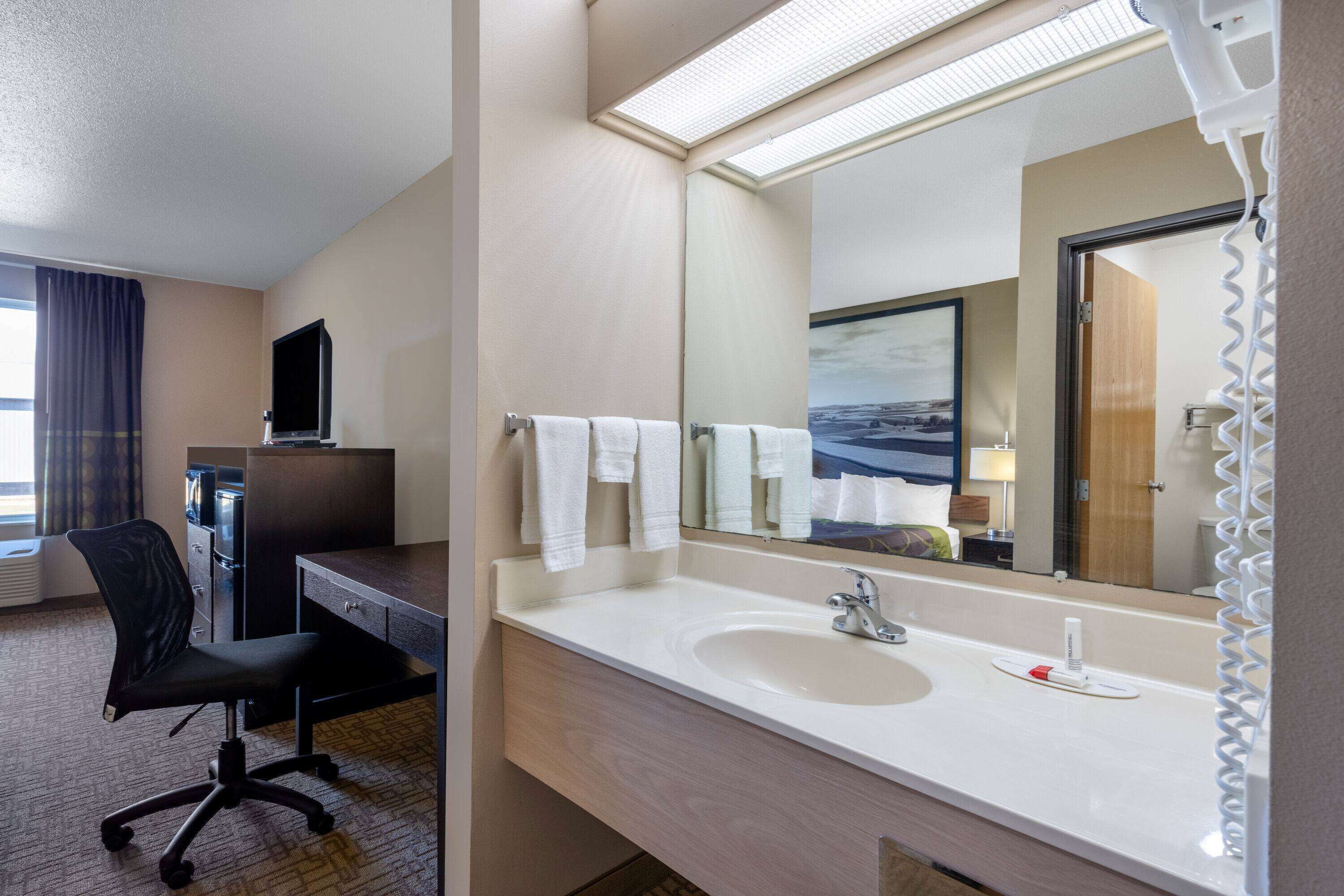 Un baño de hotel con lavamanos, espejo y una silla.