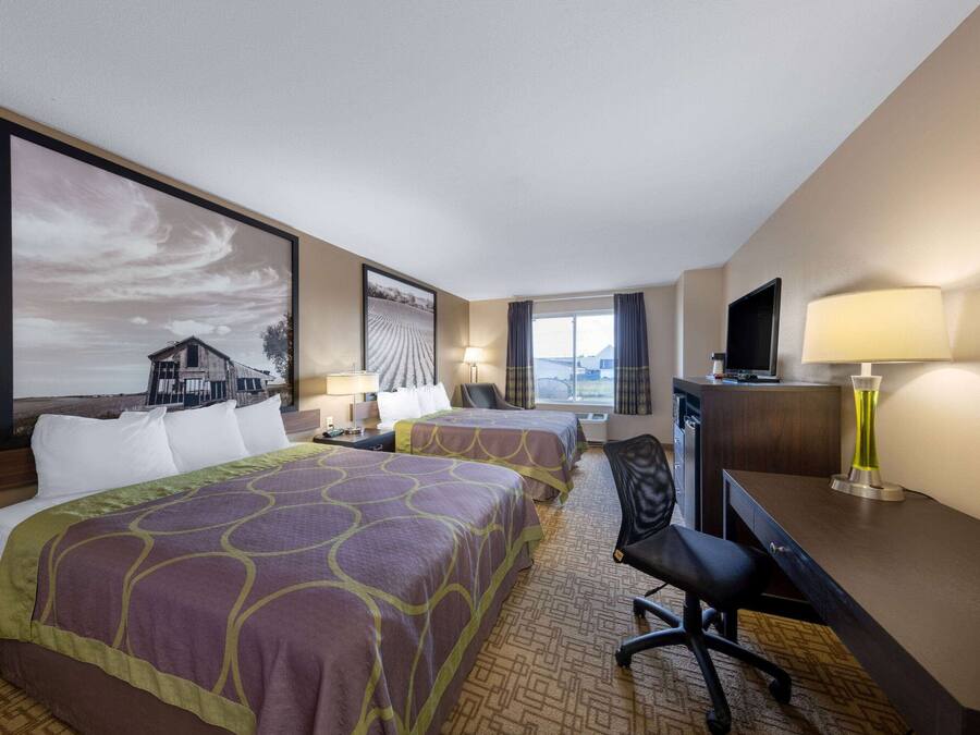 A hotel room with two beds, a desk, a chair, a TV, and a large window.