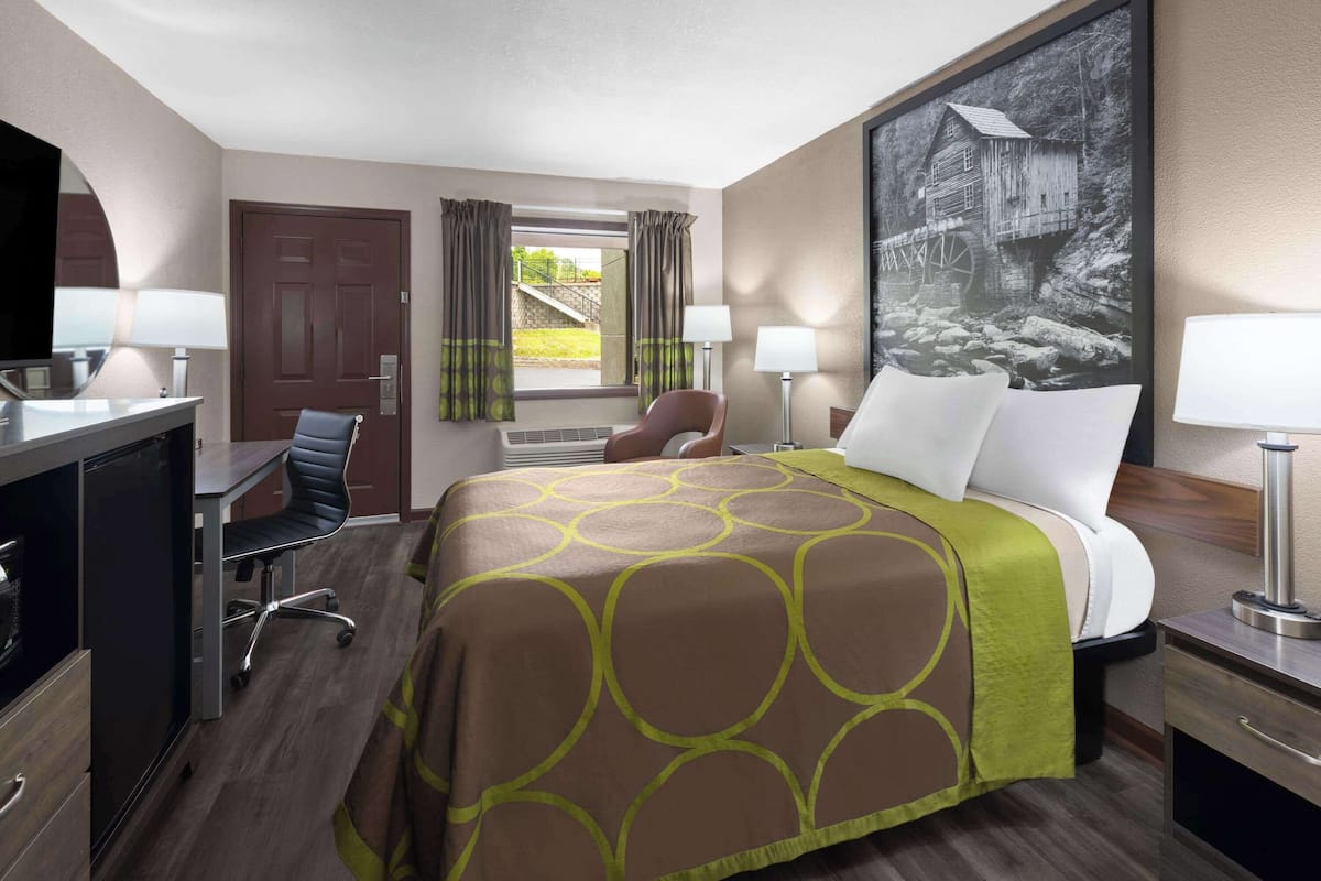Una habitación de hotel con cama, escritorio, silla y un ventanal con cortinas.