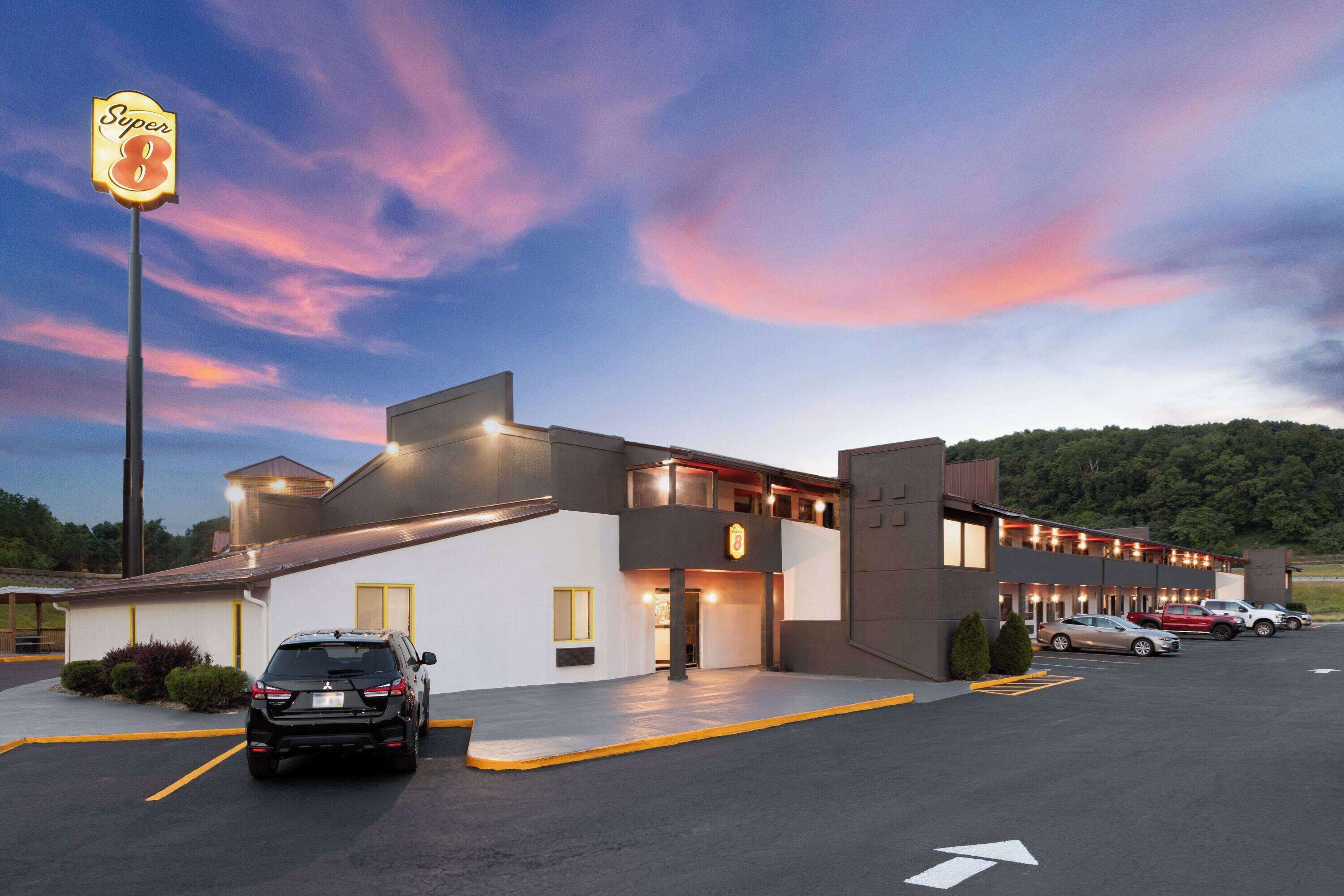 A Super 8 motel with a two-story structure, a parking lot, and a scenic sunset backdrop.