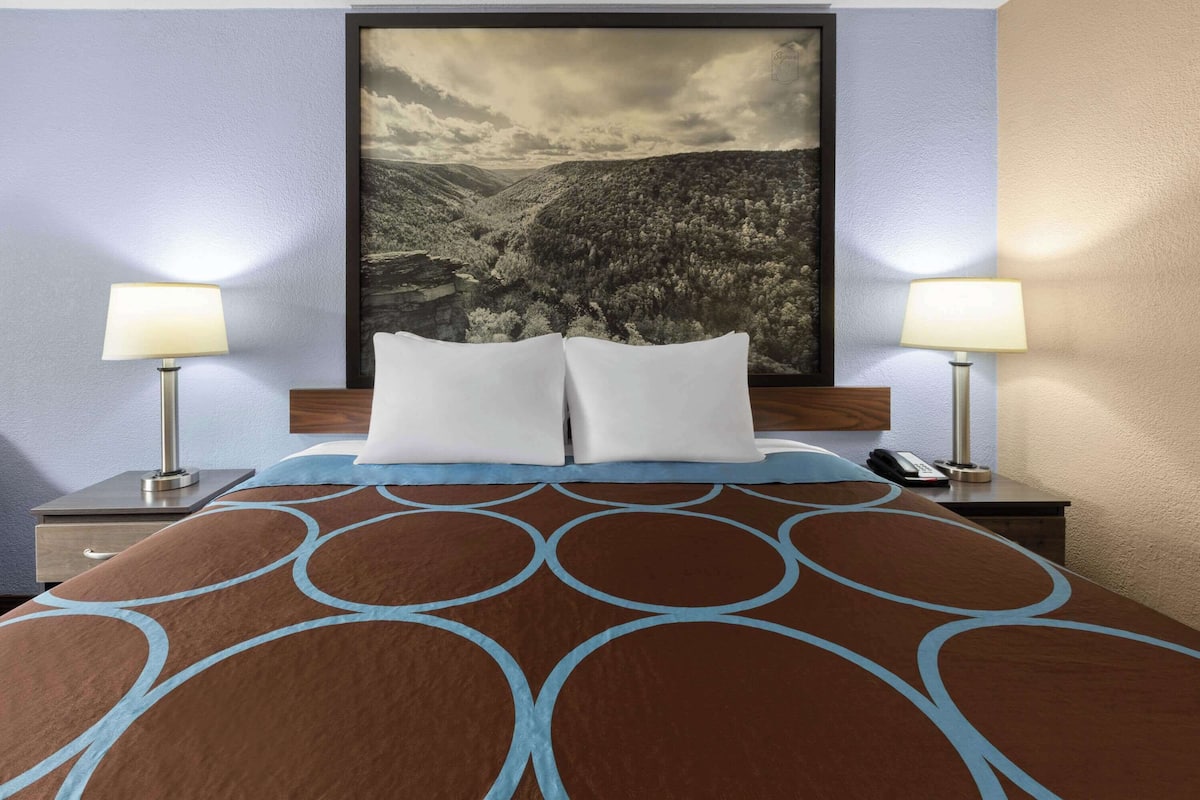 Habitación de hotel con cama, dos lámparas de noche, mesita de noche con teléfono y un cuadro grande enmarcado en la pared.