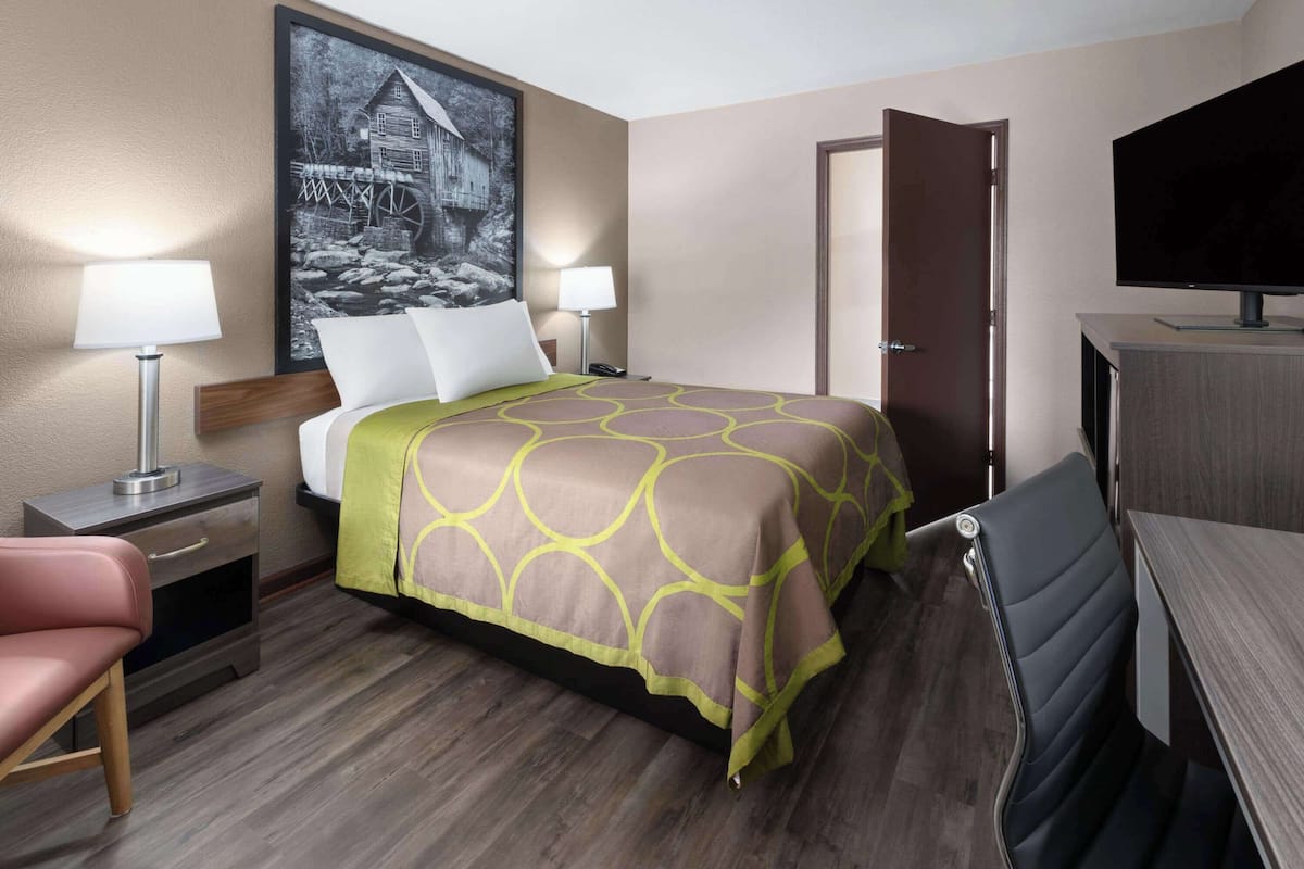 Una habitación de hotel con una cama, mesitas de noche, un escritorio, una silla, un televisor y un cuadro en la pared.