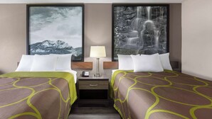 Habitación de hotel con dos camas, una mesita de noche con lámpara y dos cuadros en las paredes.