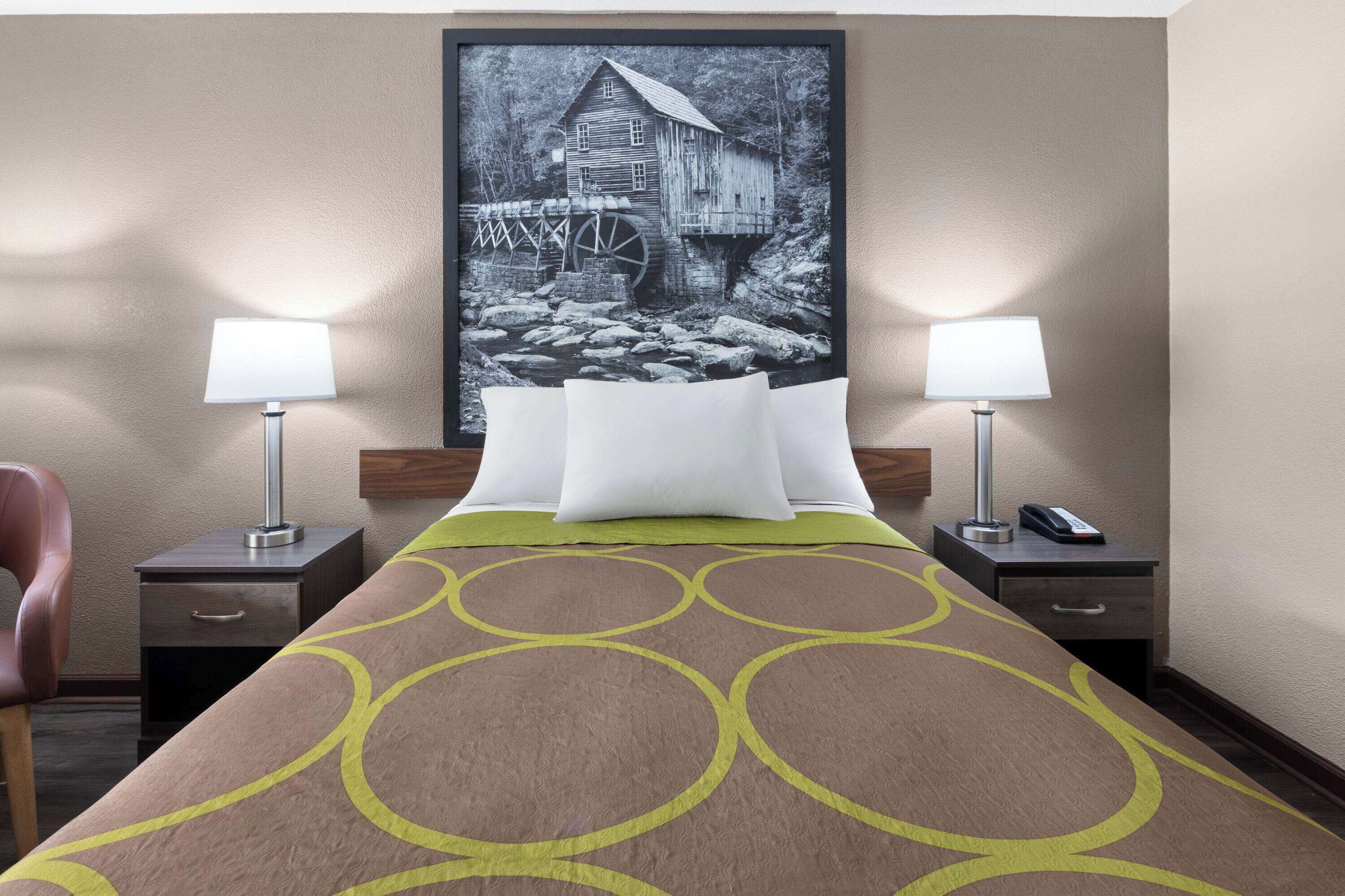 A hotel room with a bed, two bedside tables with lamps, a chair, and a large framed picture on the wall.