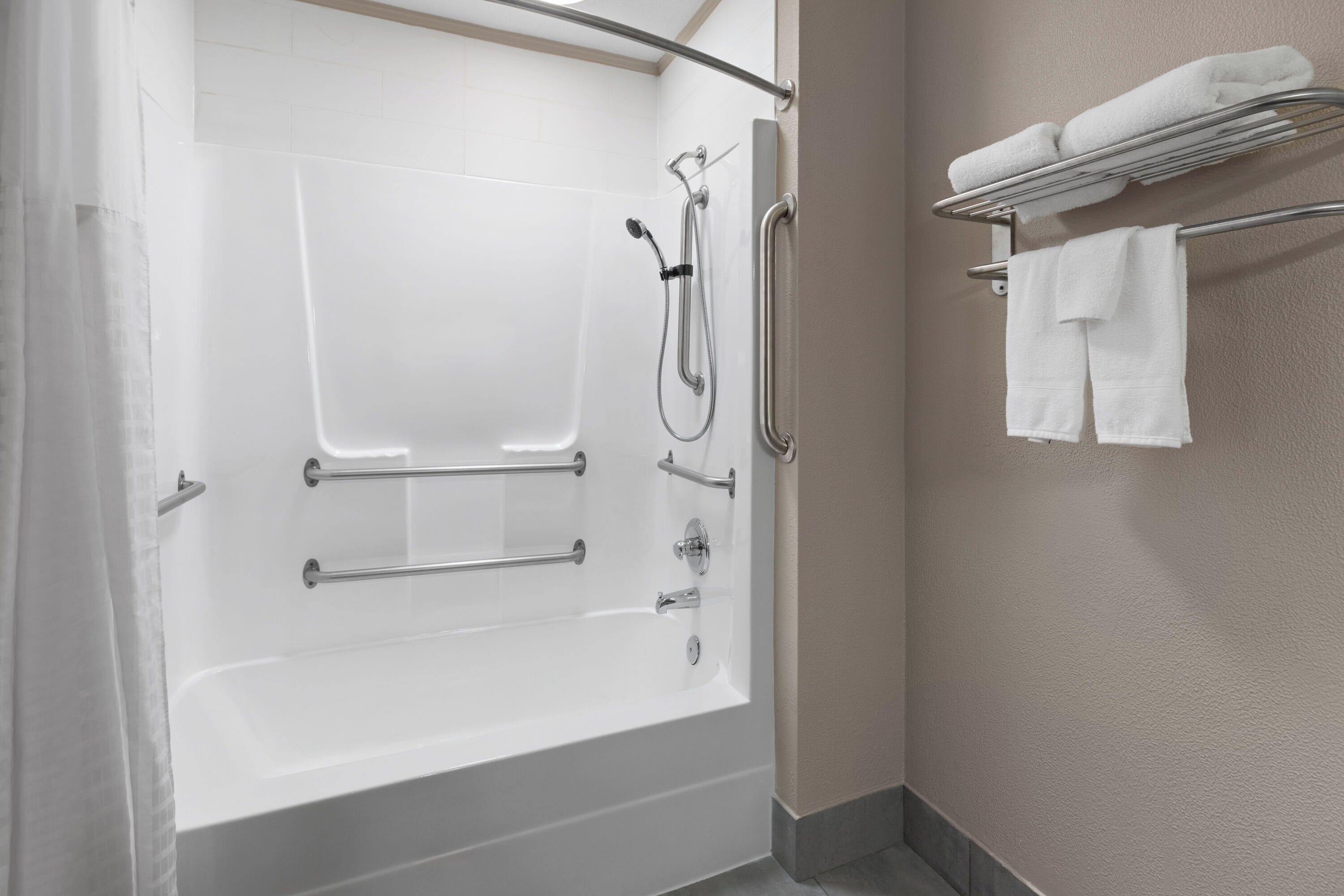 A modern bathroom with a walk-in shower, grab bars, and a towel rack.