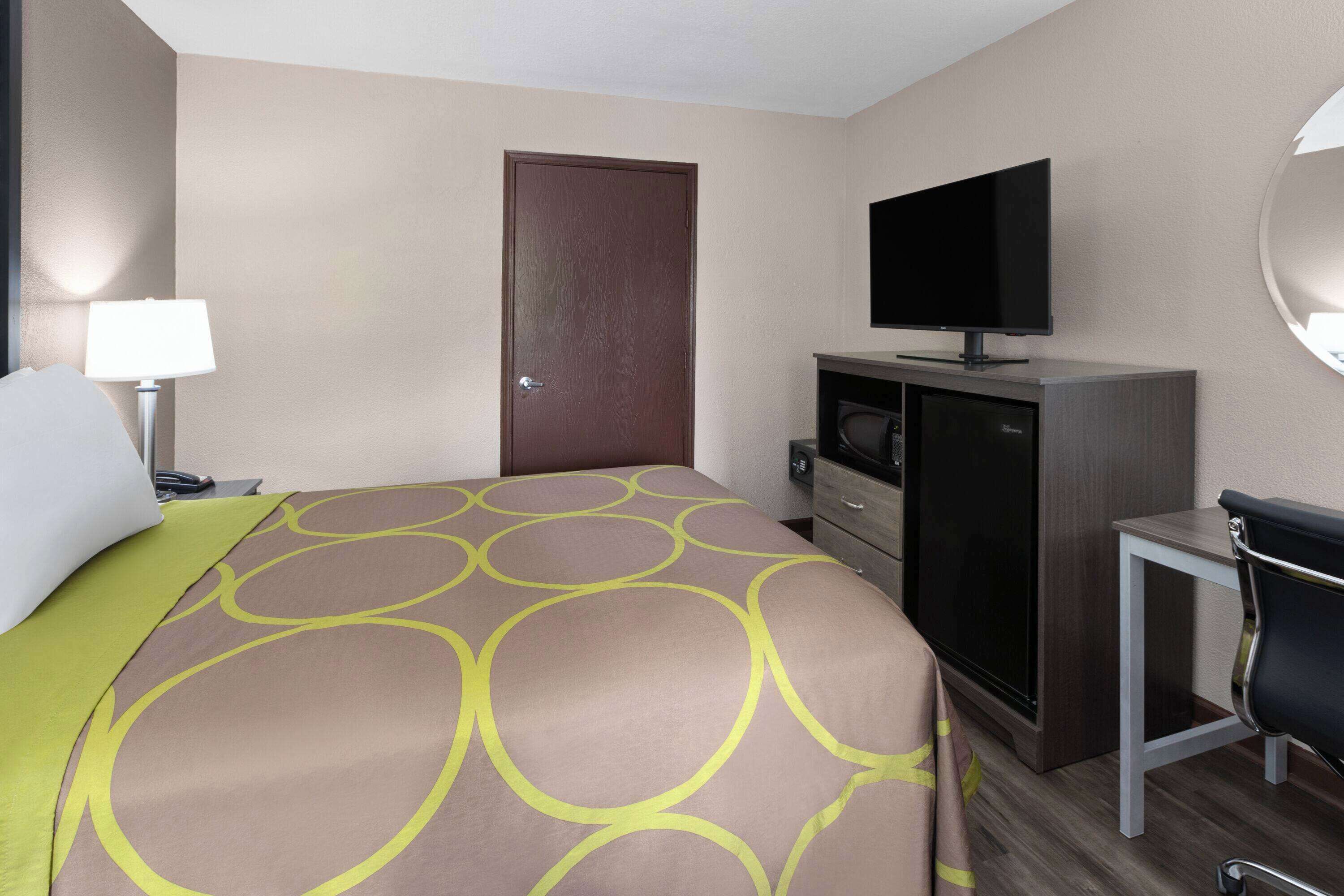 A hotel room with a bed, a television, a desk, and a door.