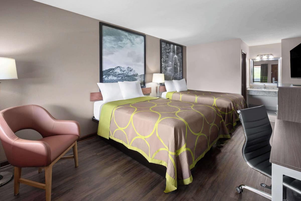 Habitación de hotel con una cama, dos mesitas de noche, un escritorio con silla, una lámpara y un ventanal grande.