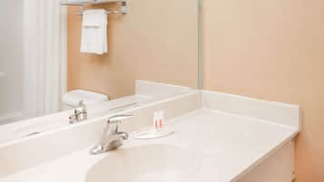 Casa de banho com lavatório branco, torneira cromada e espelho. Tem um porta-toalhas com toalha e uma pequena estante com suporte para escova de dentes.