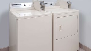 A pair of white front-loading washers with control panels, installed in a corner of a room with tiled flooring. - Super 8 by Wyndham Shipshewana (Shipshewana)