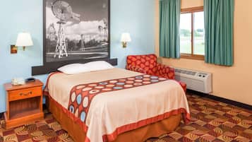 A hotel room with a bed, two bedside lamps, a heater, a patterned carpet, and a large window with curtains.