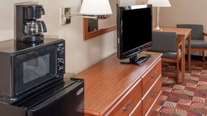 A hotel room with a microwave, coffee maker, television, wooden dresser, and a patterned carpet. - Super 8 by Wyndham Shipshewana (Shipshewana)