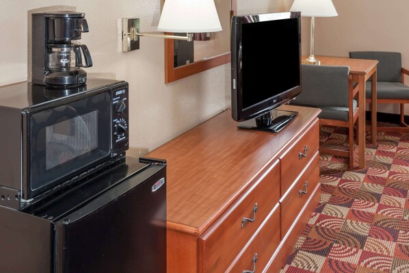 Habitación de hotel con microondas, cafetera, televisión, cómoda de madera y alfombra estampada.