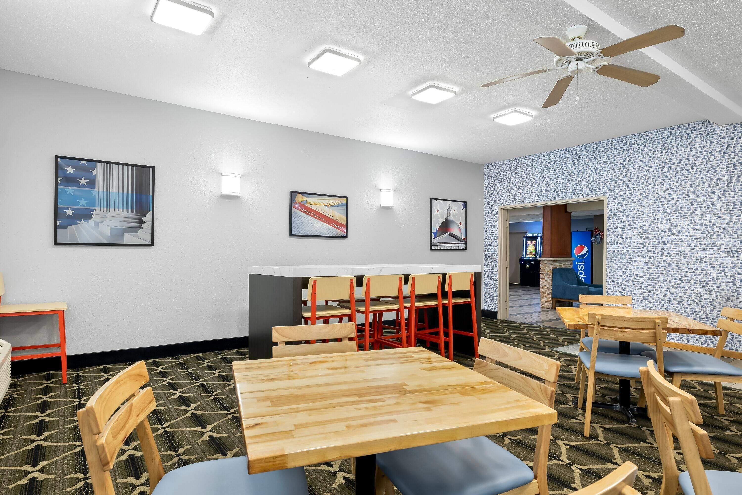 A dining area with wooden tables and chairs, a ceiling fan, and wall-mounted lights.