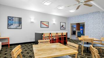 A dining area with wooden tables and chairs, a ceiling fan, and wall-mounted lights.