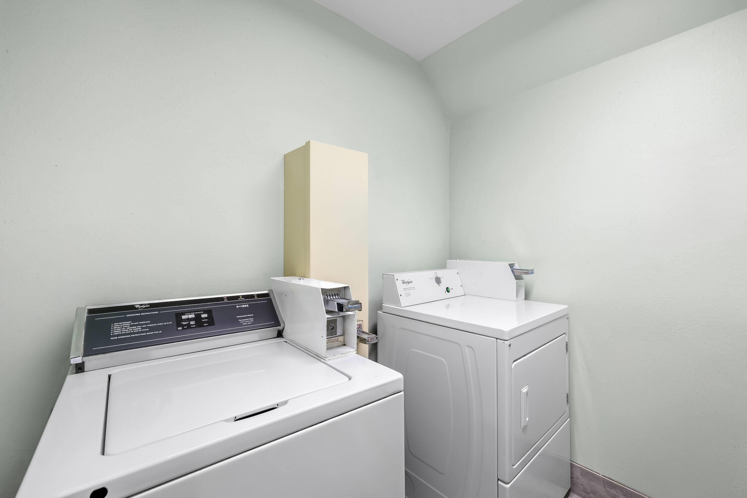 A laundry room with a front-loading washer and dryer, a tall cabinet, and a wall-mounted control panel.