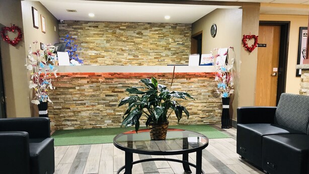 A reception area with a stone wall, a reception desk, a potted plant, and two black sofas. - AmericInn by Wyndham Columbus Wisconsin (Columbus)