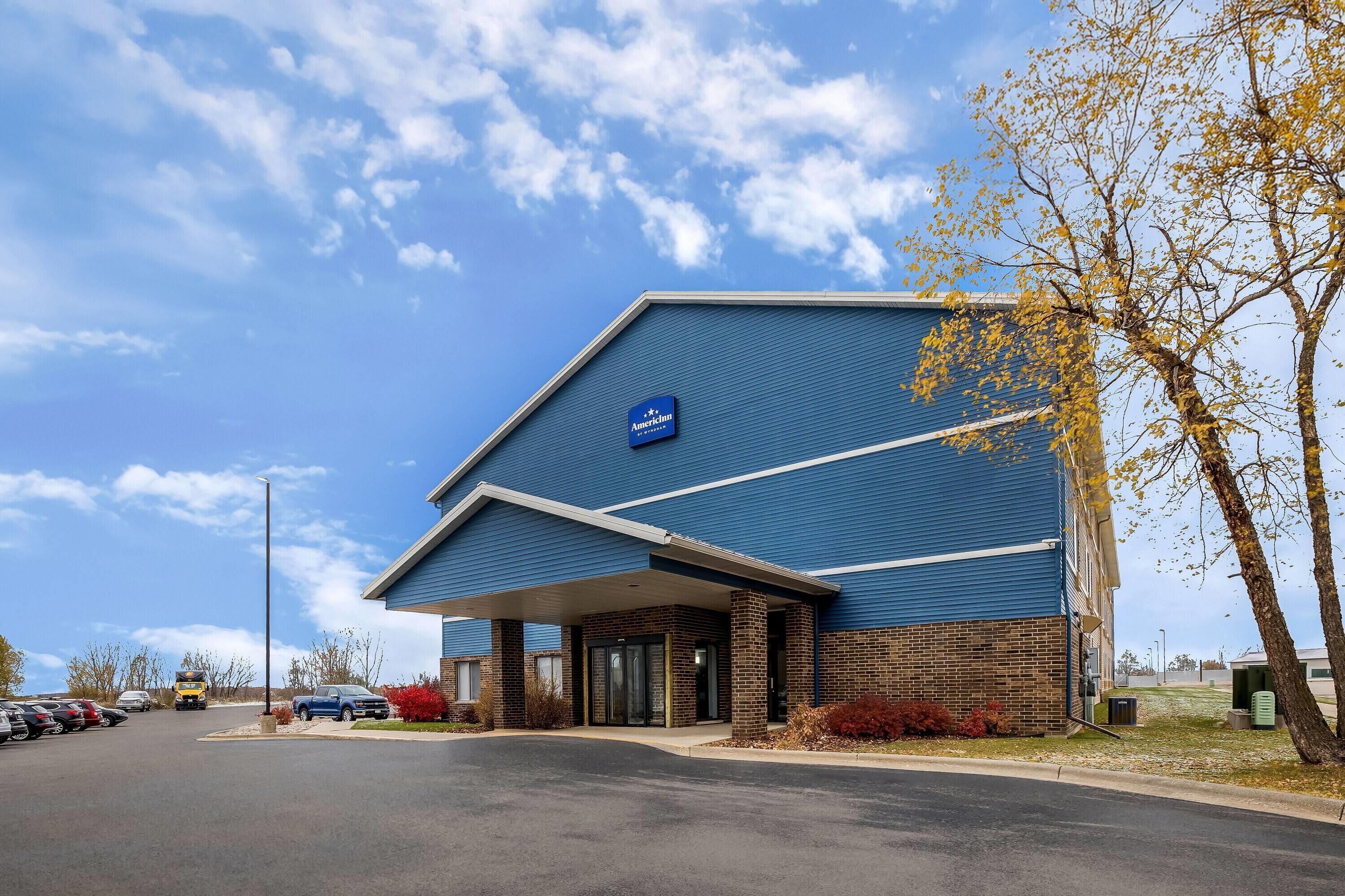A hotel with a blue exterior, a covered entrance, and a parking lot with cars.