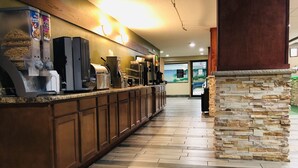 A long reception desk with a coffee machine and cereal dispensers, a stone accent wall, and a view of the lobby area. - AmericInn by Wyndham Columbus Wisconsin (Columbus)