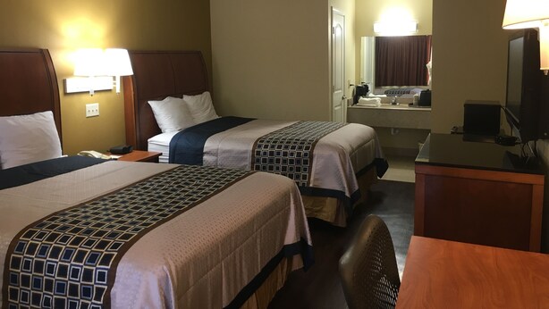 Ein Hotelzimmer mit zwei Betten, einem Schreibtisch, einem Stuhl, einem Fernseher und einem durchgegangene Tür sichtbaren Badezimmer.