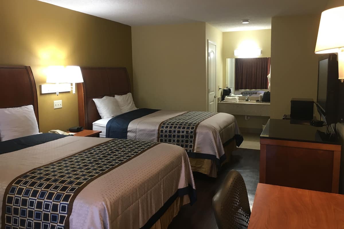 A hotel room with two beds, a desk, a chair, a television, and a bathroom visible through an open door.