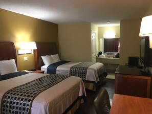 A hotel room with two beds, a desk, a chair, a television, and a bathroom visible through an open door. - Navasota Inn (Navasota)