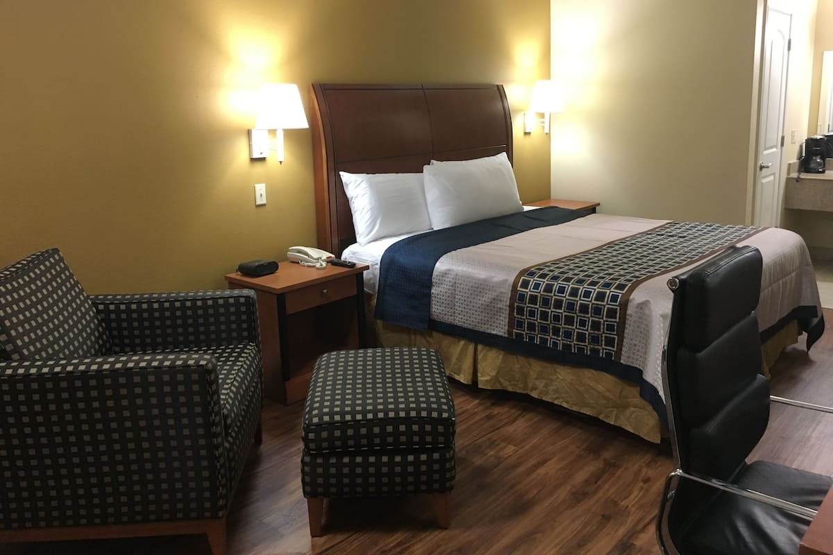A hotel room with a bed, two chairs, a nightstand, and a small table.