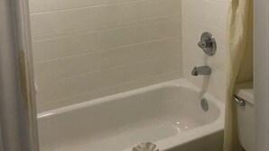 Ein Badezimmer mit weißen Fliesen, einer Badewanne, einer Duschbrause und einem WC.